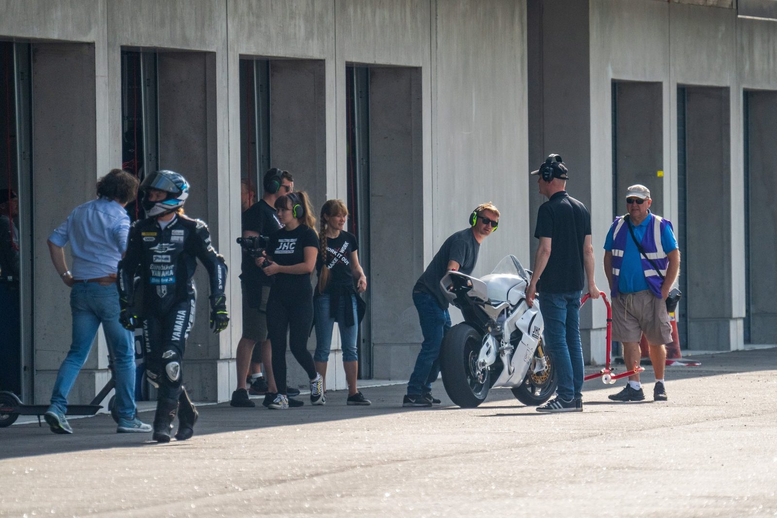 The bike being pushed back into the pit lane at KymiRing with several team members around it, a rider walking away in leathers.